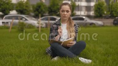 很长一段时间。 学生女孩坐在草地上，在笔记本上<strong>做</strong>笔记。 这个女孩解决了一项非常重要的<strong>任务</strong>。 4K